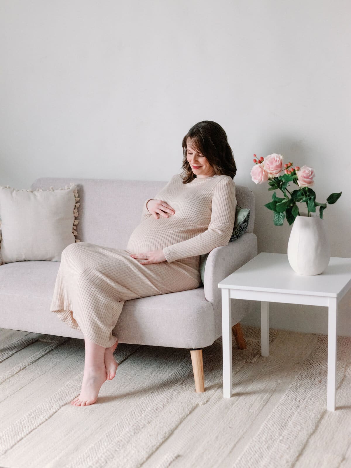 Femme enceinte sur le canapé du studio avec de belles fleurs et une jolie robe au Studio Paolina